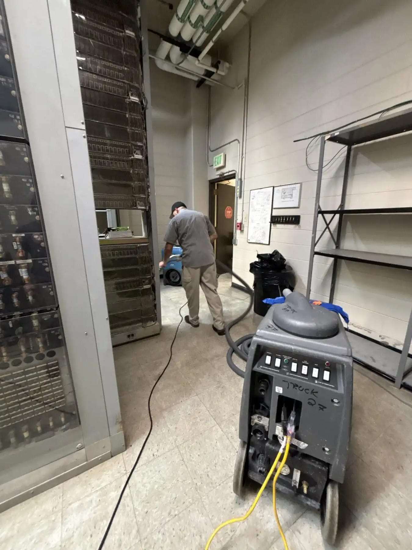 Technician with drying equipment in an industrial room with an open electrical cabinet