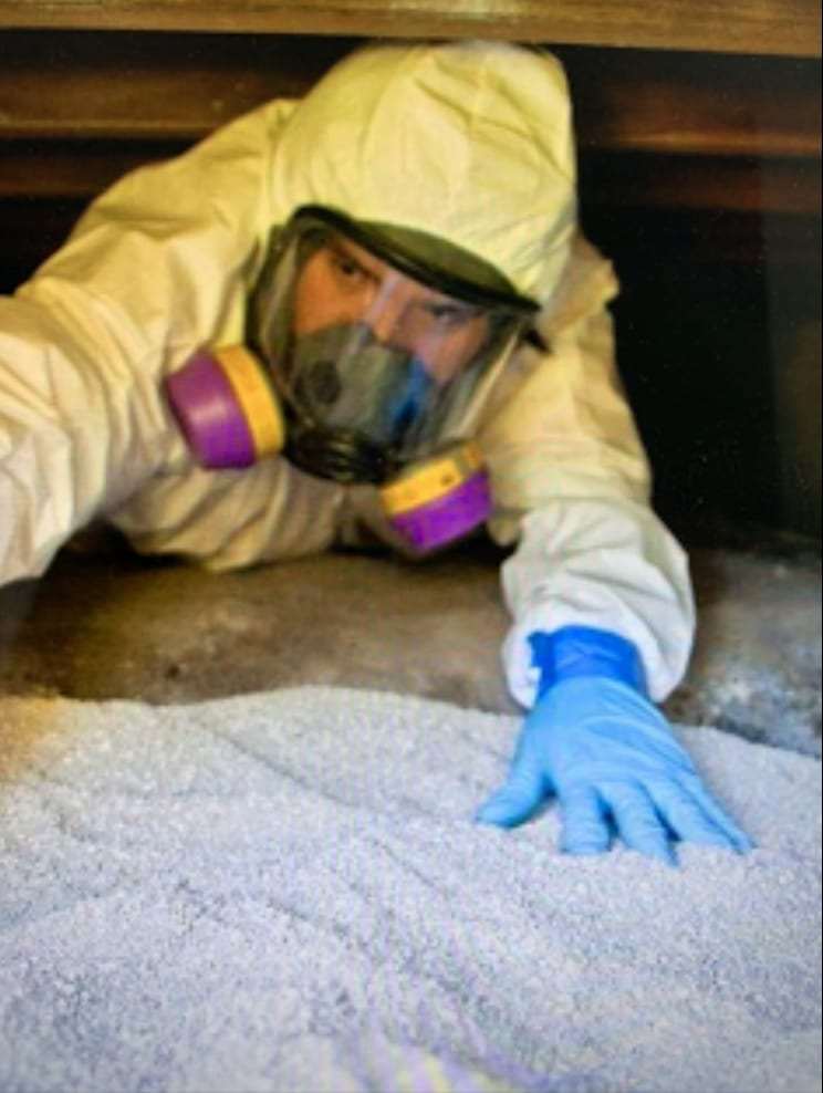 Technician in a full-face respirator working in attic insulation